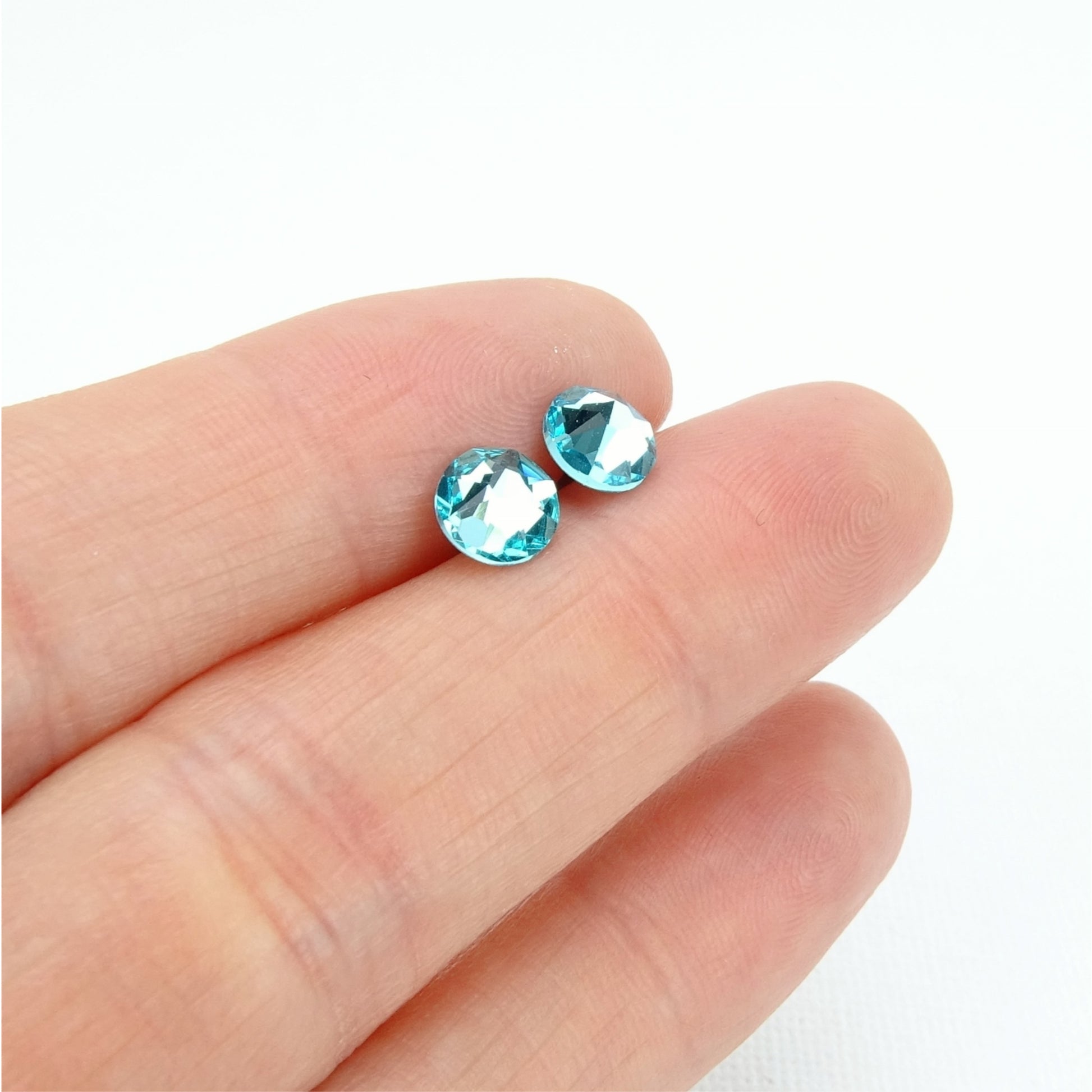 A hand holding two blue gemstones against a white background.