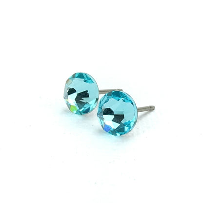 A pair of turquoise-colored earrings with a clear gemstone in the center, resting on a white background.