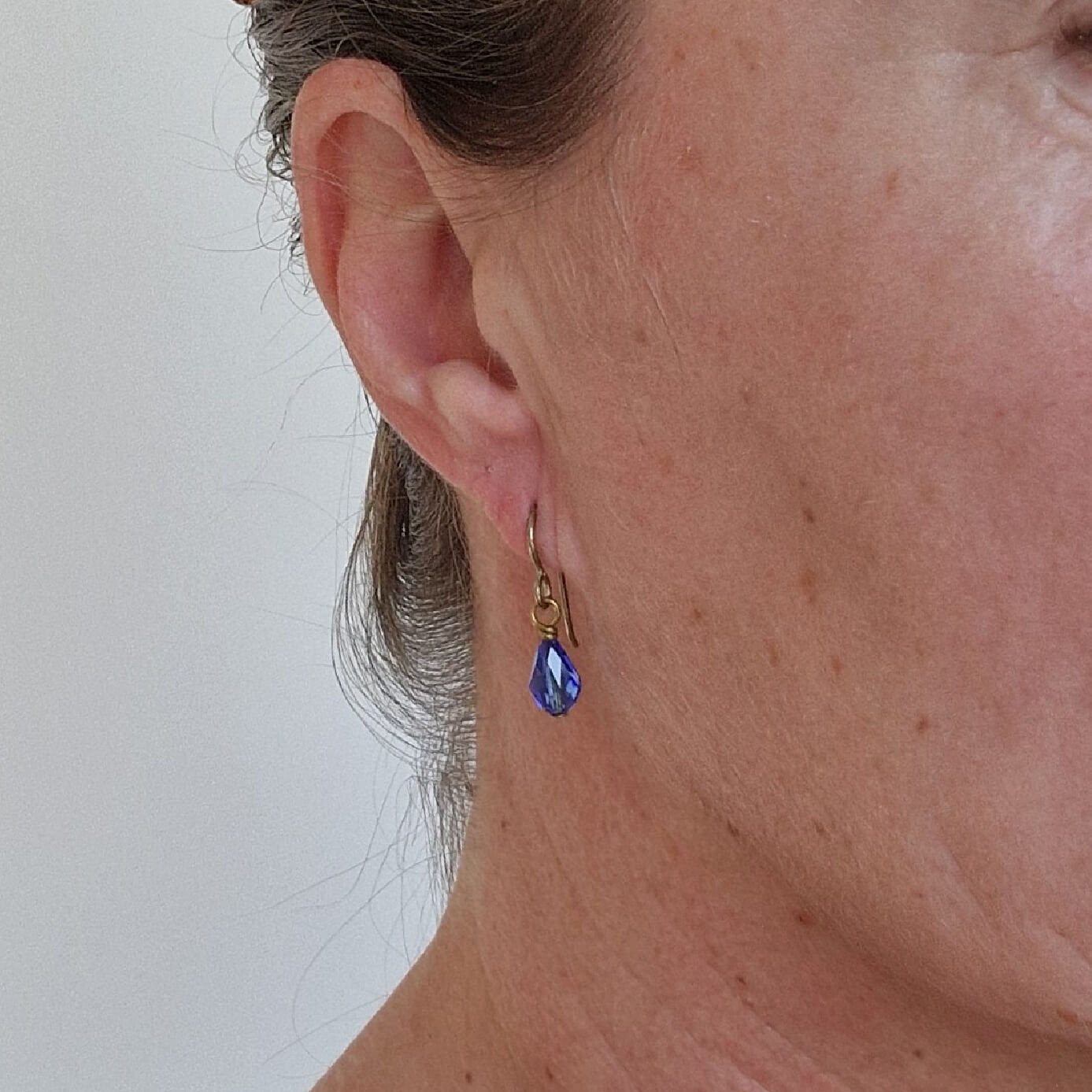 Gold Titanium Earrings with Sapphire Blue Crystal Teardrops shown in ear