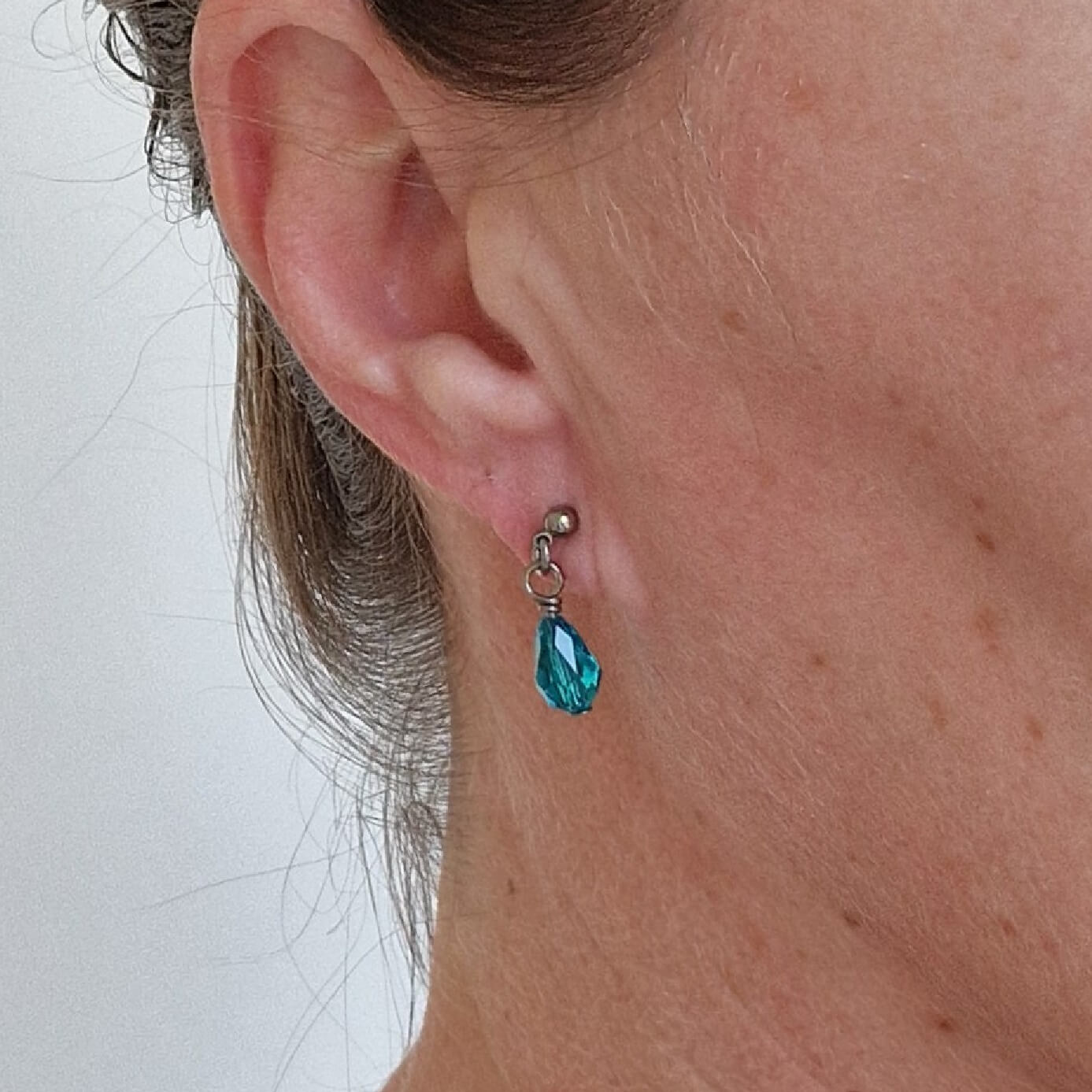 Titanium Stud Earrings with Dangling Blue Zircon Crystal Teardrops Shown on Ear