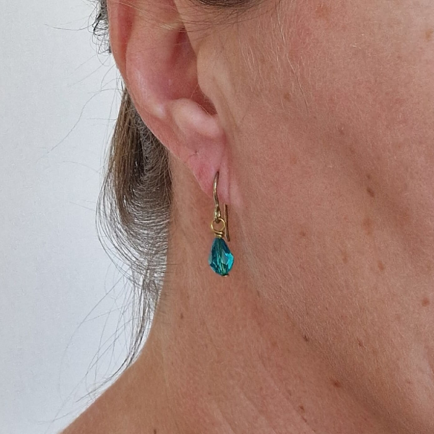 Gold Titanium Earrings with Blue Zircon Crystal Teardrops Shown in Ear